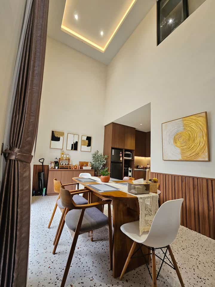 Light brown wood tone and white-walled dining room featuring terrazzo floor and high ceiling in cozy open kitchen space