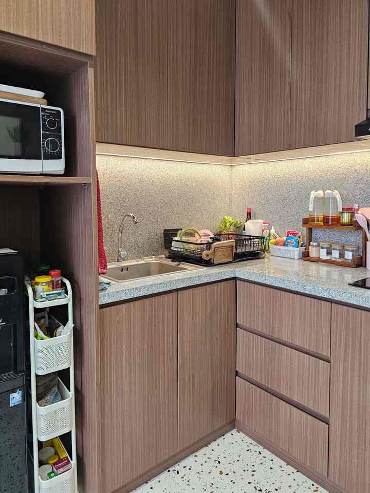 Wood tone compact kitchen featuring sink, storage racks, and microwave with practical layout