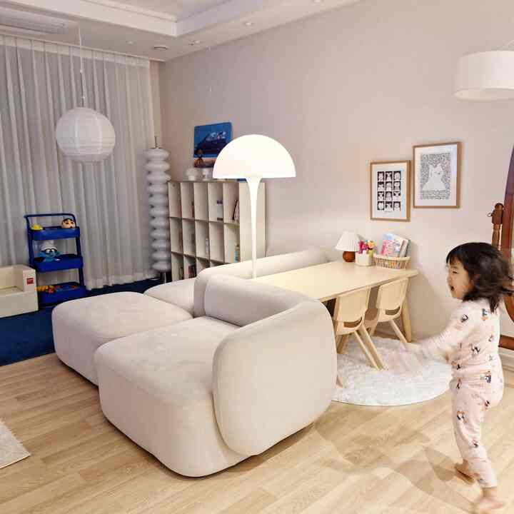 ナチュラルカラーと木目調が調和した子供部屋兼リビングスペース、大きなクリーム色のソファと子供用テーブルが配置された温かみのある雰囲気のインテリア