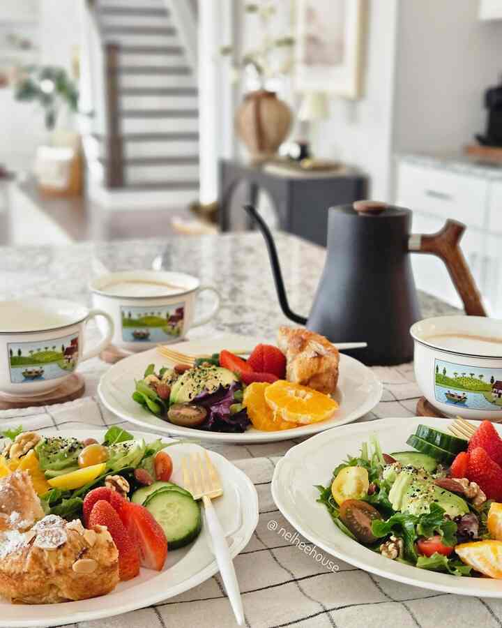 Bright white-toned kitchen dining table featuring home cafe coffee setup with fresh fruit and salad plated for cozy weekend brunch