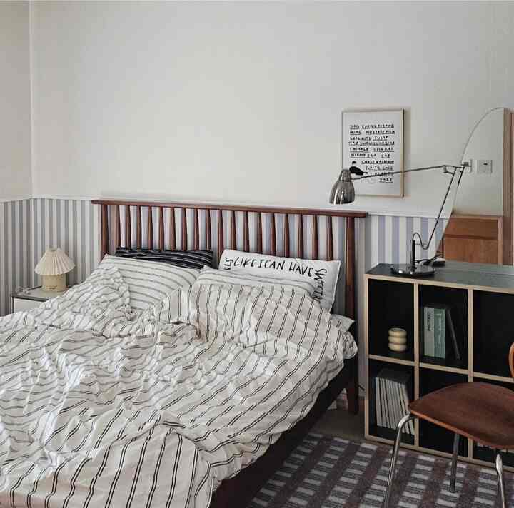 White walls and brown wooden bed frame with striped duvet cover and nightstand in a simple natural modern bedroom