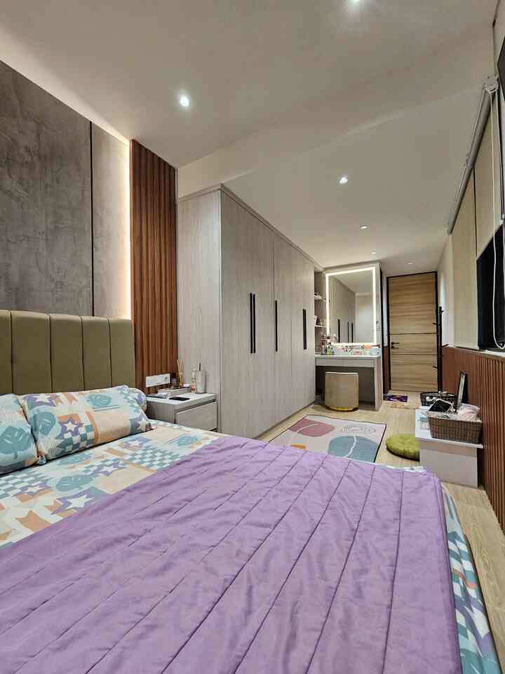 Long and narrow bedroom with natural wood tones and light gray elements, featuring a purple bedspread, built-in wardrobe, and illuminated wall panel creating a cozy atmosphere