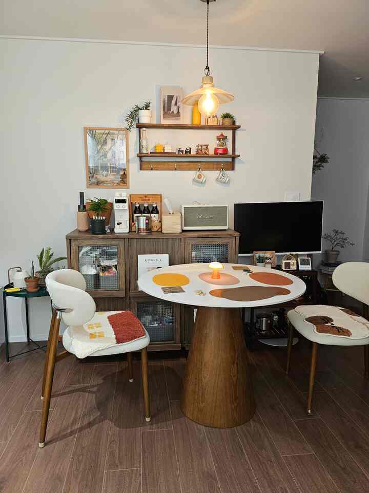 ナチュラルなブラウンとホワイトのトーンの円形ダイニングルーム、円形セラミックのダイニングテーブルと椅子、壁の棚と収納キャビネットが調和した温かみのある空間