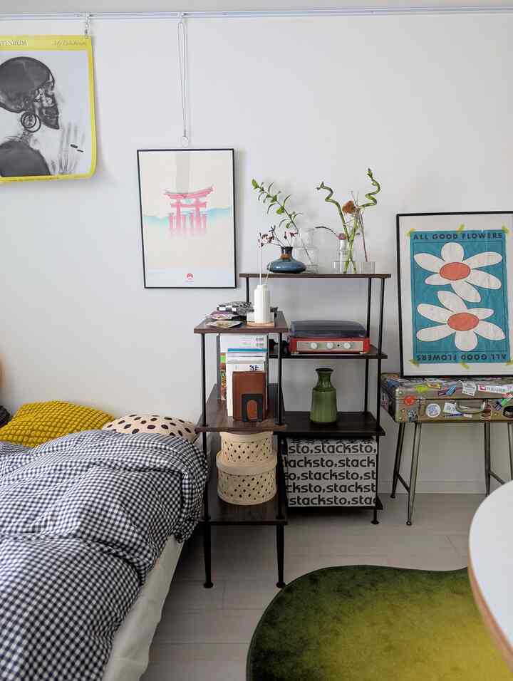 白い壁とチェック柄のベッドカバー、木製と黒のラックが配置されたナチュラルな雰囲気の寝室