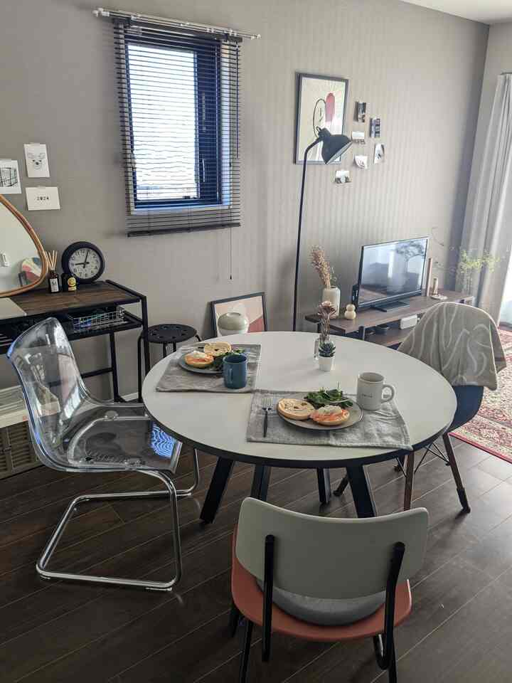 木目調の床と白い丸テーブルが並ぶ二人用ダイニングルーム、透明な椅子と黒いフロアランプが調和する自然な雰囲気のインテリア