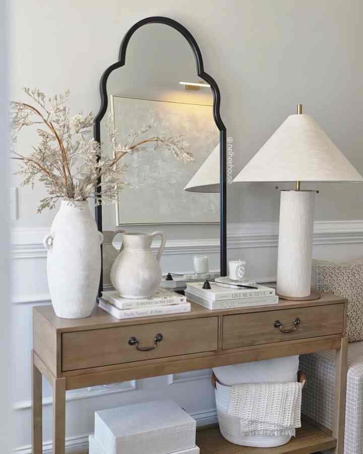 Beige and natural-toned entrance featuring a black arched mirror and wooden console table, complemented by elegant lamp and decor for a minimal warm look