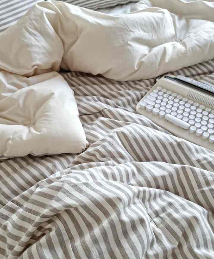 アイボリーとグレーのストライプ柄の寝具とレトロ風のミニキーボードが配置された温かみのある寝室のインテリア