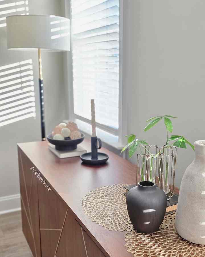 Bright modern living room with wood tone cabinet featuring white floor lamp and assorted decor by a sunlit window