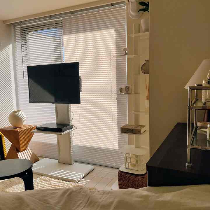 白とベージュの落ち着いた色調の寝室、テレビ台とミニマルな家具が配置された印象的な一人暮らし空間