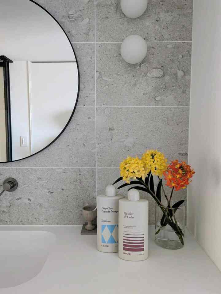 White and gray toned bathroom featuring a round mirror and a vase with vibrant flowers, creating a clean and natural interior