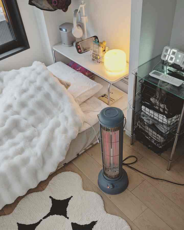 白と木目調のワンルーム寝室、コンパクトなカーボンヒーターとミニマルなディフューザーが置かれた温かみのあるインテリア