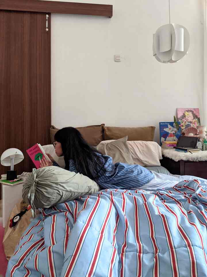 White-walled bedroom with brown wooden door, blue striped bedspread and cozy pillows forming a comfortable reading nook
