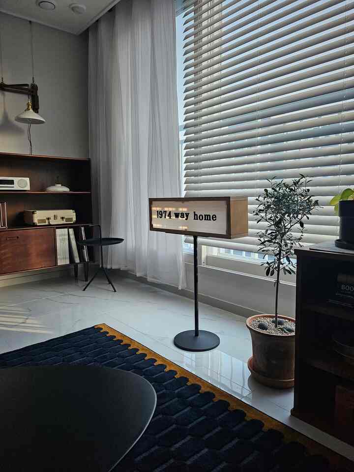 白と木目調の調和が美しいリビング、木製の本棚やブラインド、モダンな照明が配置された雰囲気のある空間