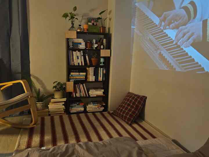 温かみのある木目調とベージュ色のワンルーム読書スペース、本棚とチェック柄ラグ、クッションが落ち着きを演出