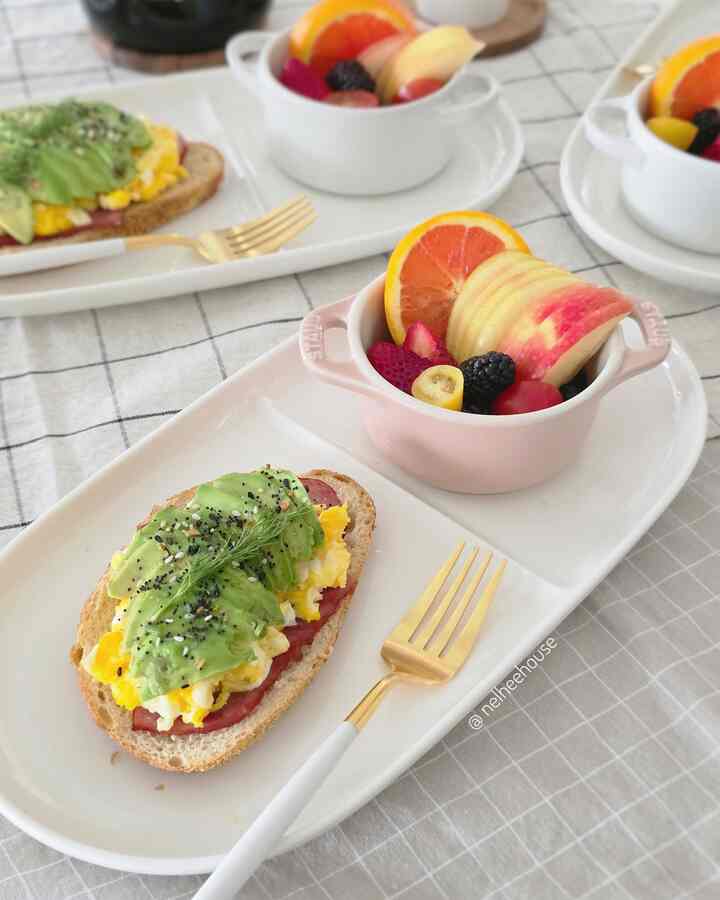 Minimal white-toned dining setting with white plates featuring avocado toast and fruit bowls on a clean brunch table