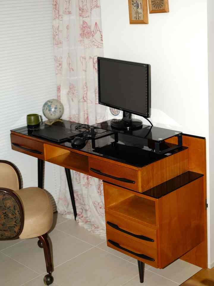 Compact workspace featuring a wood-toned desk with black glass top, a monitor, and an office chair arranged neatly