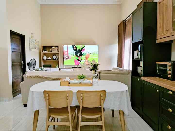 Natural and simple living and dining room in beige and brown wood tones featuring dining table, sofa, kitchen cabinets, and TV