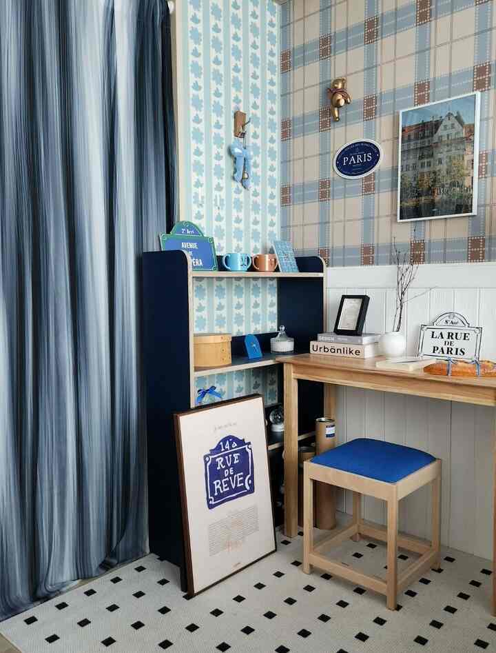ブルートーンのカーテンとデスク、スツール、多彩な壁紙で飾られたフレンチカントリースタイルの小さな書斎空間