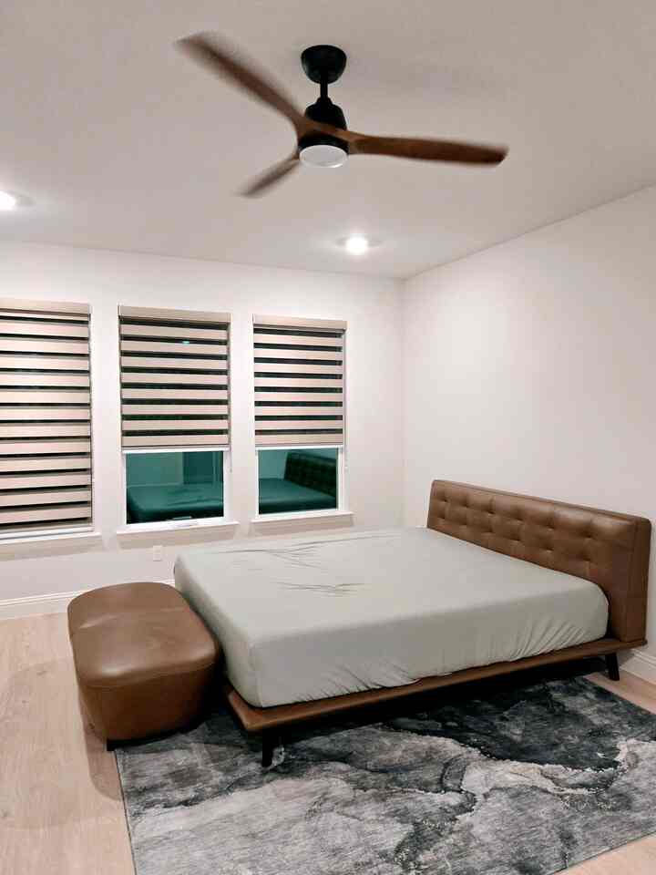 Cozy bedroom with white walls featuring brown bed, ottoman, and ceiling fan with light fixture