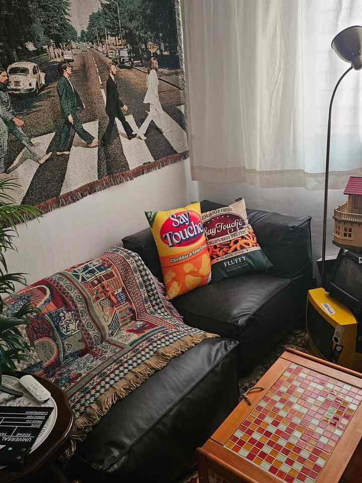 ヴィンテージな雰囲気のリビング、黒いソファと多彩なファブリック、壁にビートルズのタペストリーが配置されたインテリア