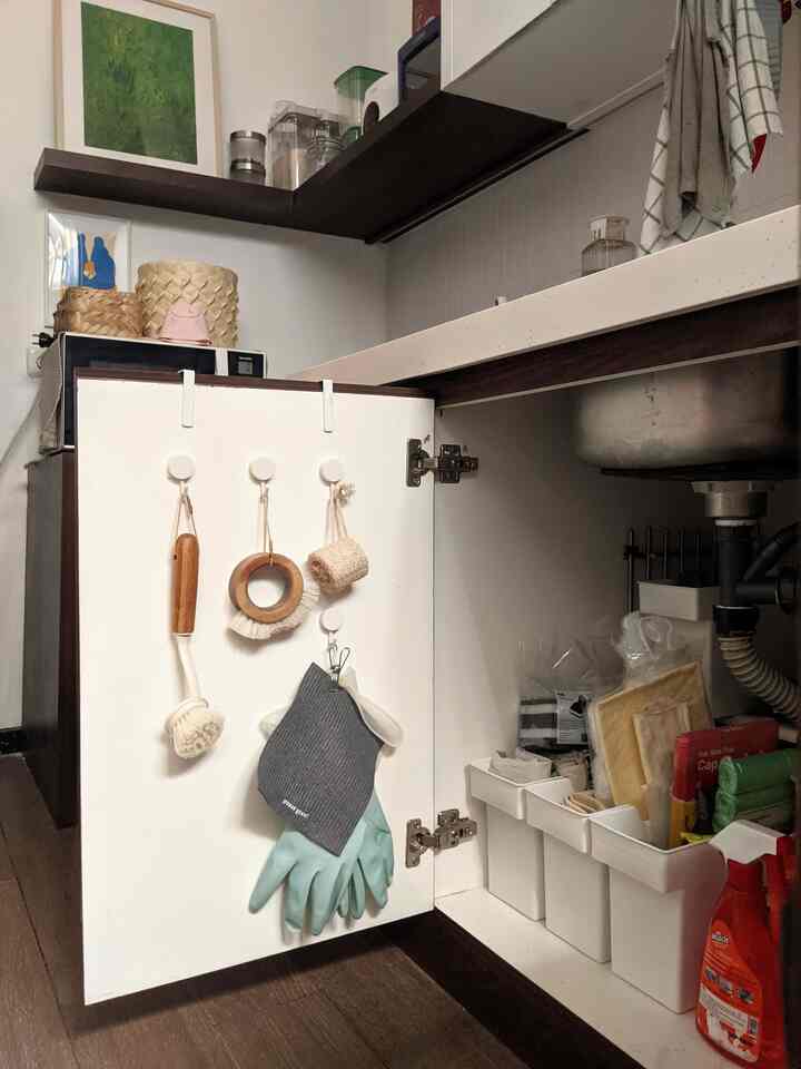White and brown toned kitchen space featuring an open cabinet with organized cleaning tools, showcasing a practical and neat area