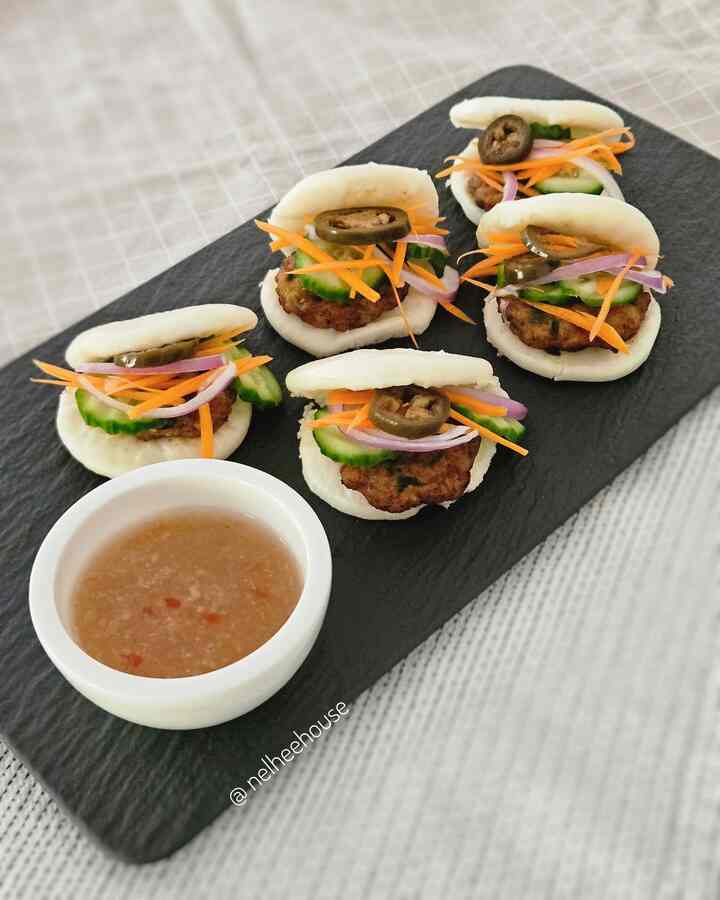 White and black toned kitchen table featuring neatly arranged small buns with sliced toppings and a bowl of dipping sauce
