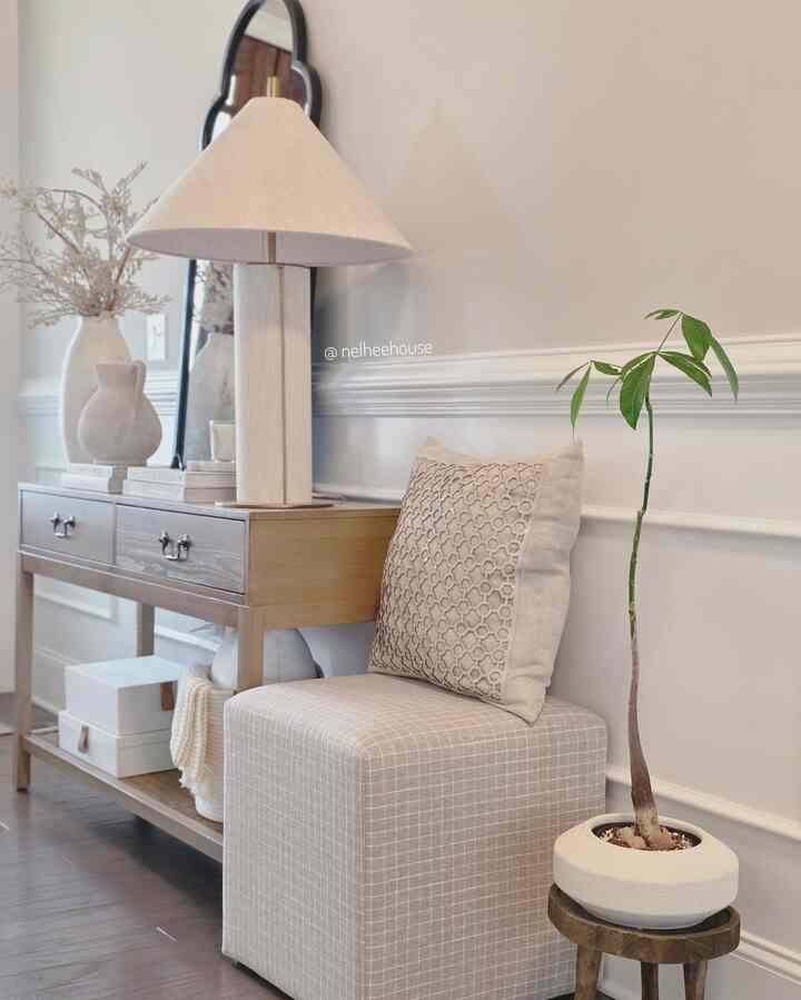 Beige and natural-toned entrance space featuring an ottoman, console table with linen table lamp creating a cozy atmosphere
