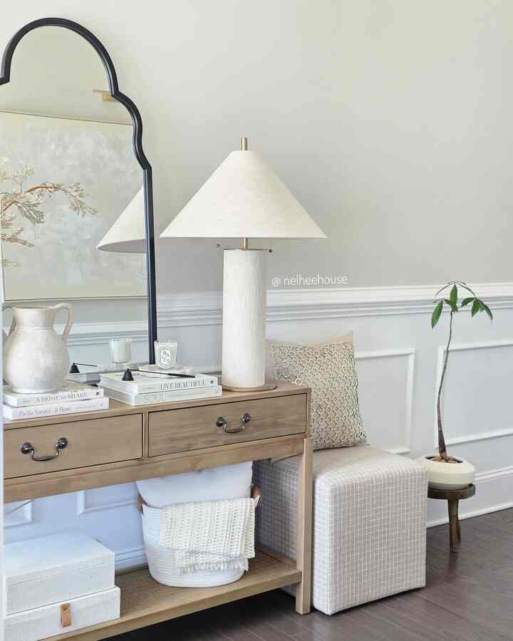 Neutral white and brown toned entrance featuring a console table with mirror, ottoman, and plant in a cozy setting