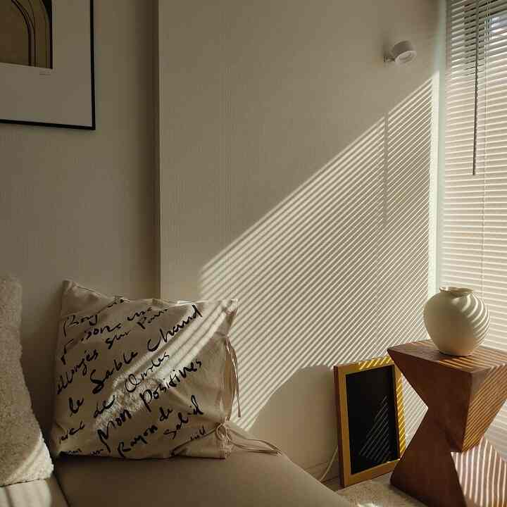 ベージュとナチュラルカラーのリビング、クッションと木製サイドテーブル、花瓶が配置された温かみのある印象的な空間