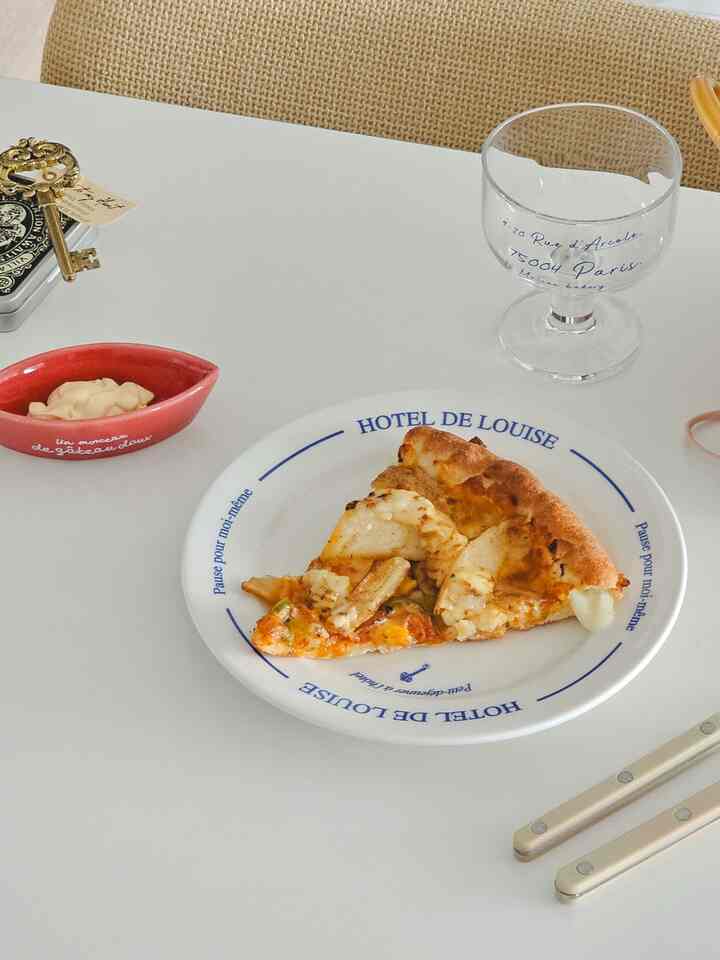 White-toned dining table featuring a plate with pizza slices and a wine glass in a cozy setting