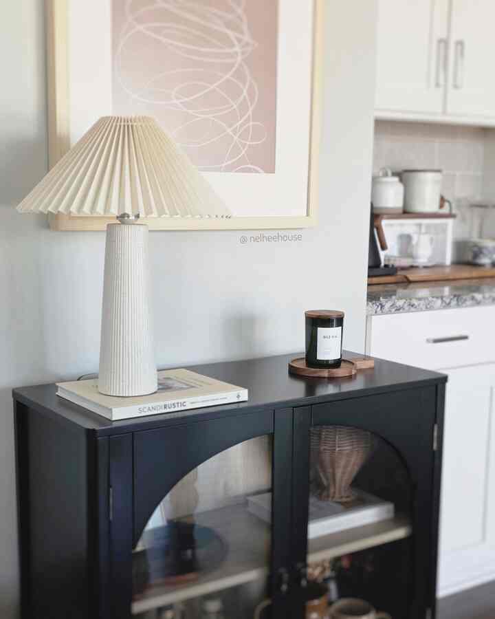 Beige and ivory toned dining room featuring a black cabinet topped with an ivory pleated table lamp and candle, creating a modern minimal space
