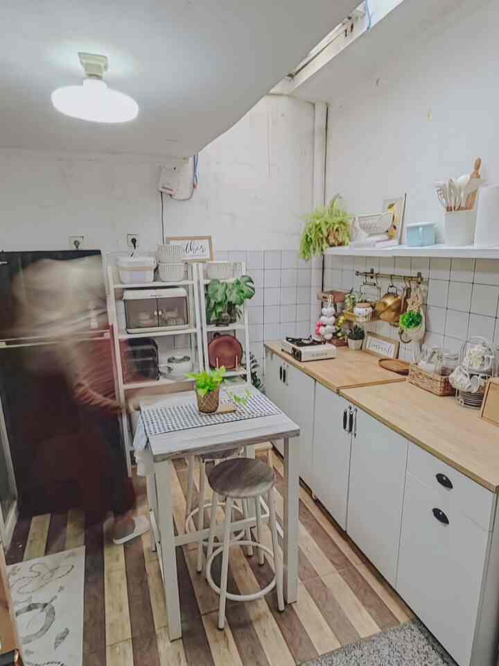 Bright white and wood tone small kitchen featuring cabinets, shelves, a compact table with stools, creating a clean functional interior