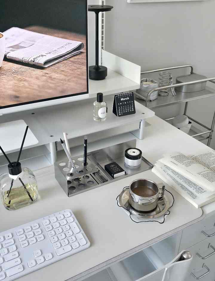 白とシルバーのトーンのモダンでミニマルなホームオフィス空間、デスクにステンレスのティーカップやディフューザーなどの整然としたアイテムが配置された雰囲気のあるインテリア
