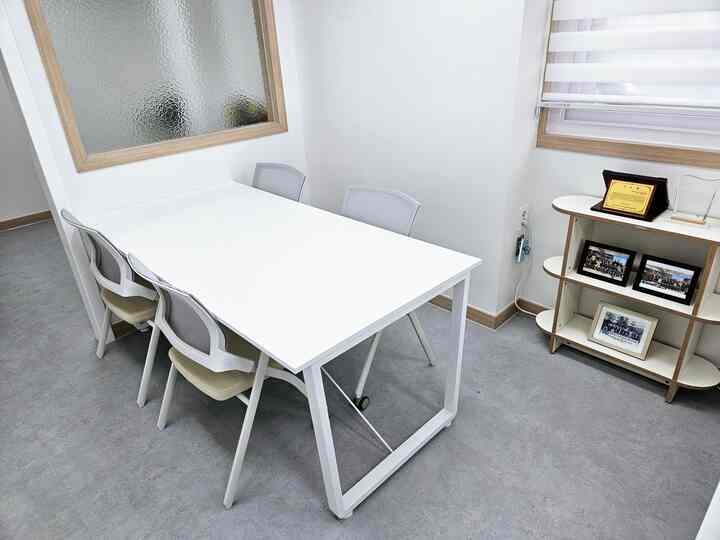 ホワイトとグレーのトーンの小さな会議室、4人用の白い会議用テーブルと椅子が配置された清潔で効率的な空間