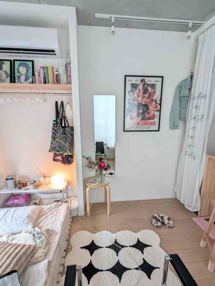 白と木目調のワンルーム寝室、ナチュラルなインテリアとポスター、花が飾られたスツールのある落ち着いた空間