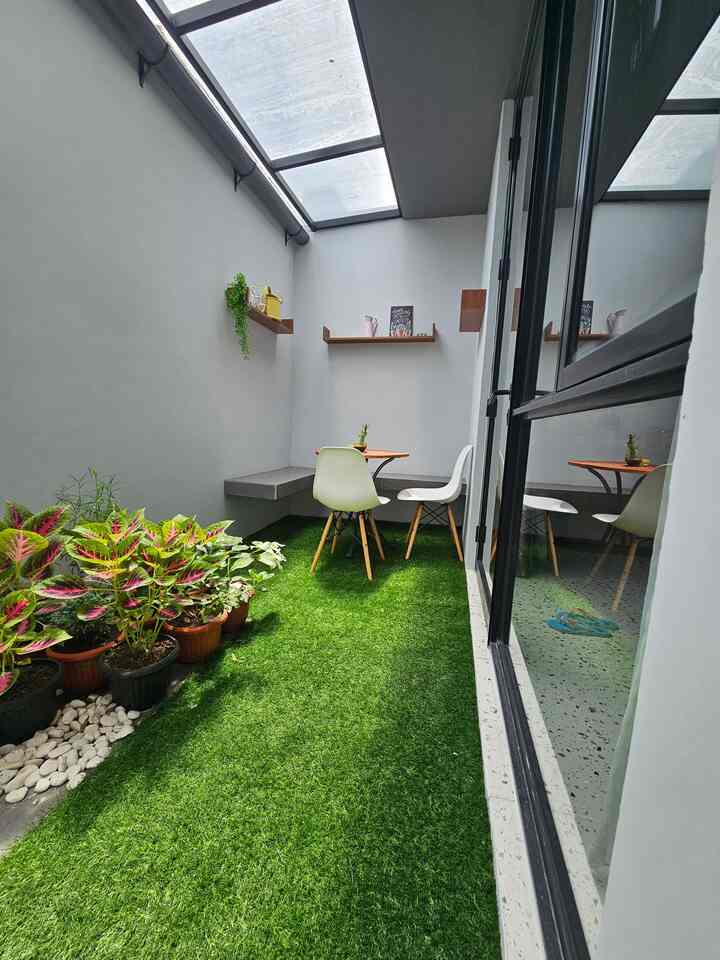 Bright balcony space with green synthetic grass carpet, plants along left side, wooden floating shelves, and a small dining table set for a natural atmosphere
