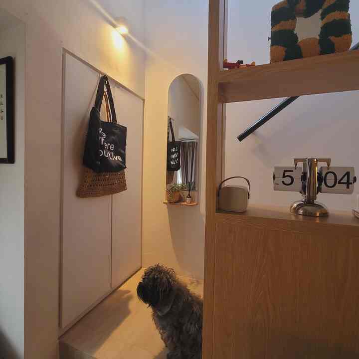 An entrance space with white walls and wood tone shelves, featuring a dog sitting on the floor and a vintage clock creating cozy ambiance