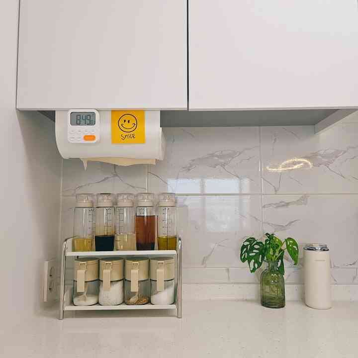 White and green toned kitchen featuring a minimal metal shelf neatly organized with spice containers and bottles, creating a clean space