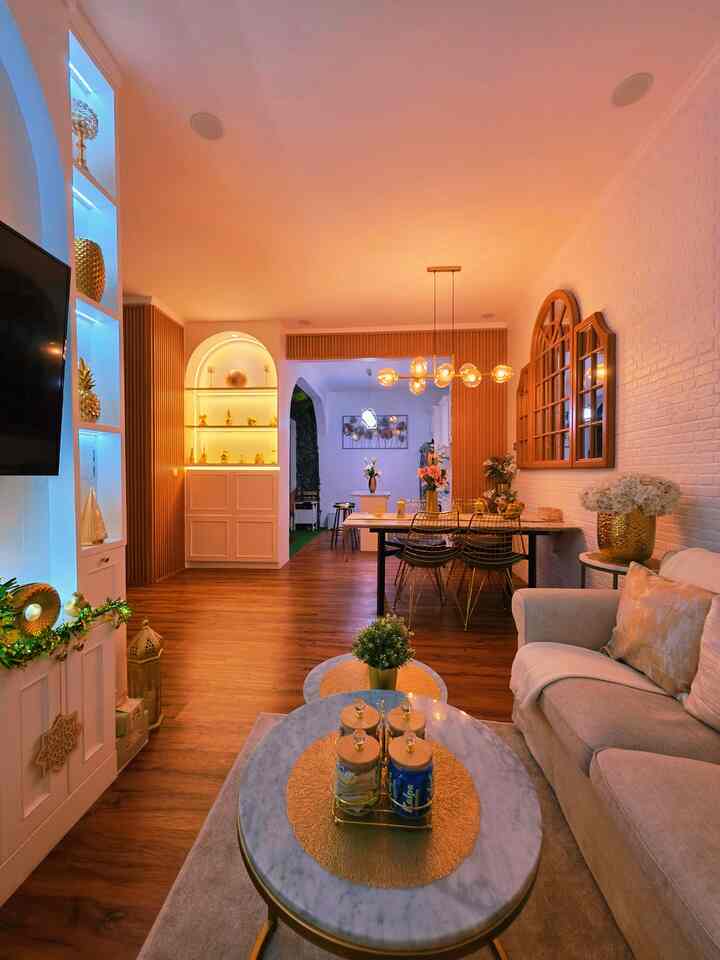 Warm wood tones and gold accents define this open-plan living and dining area, featuring a comfortable sofa and pendant lighting for a cozy atmosphere