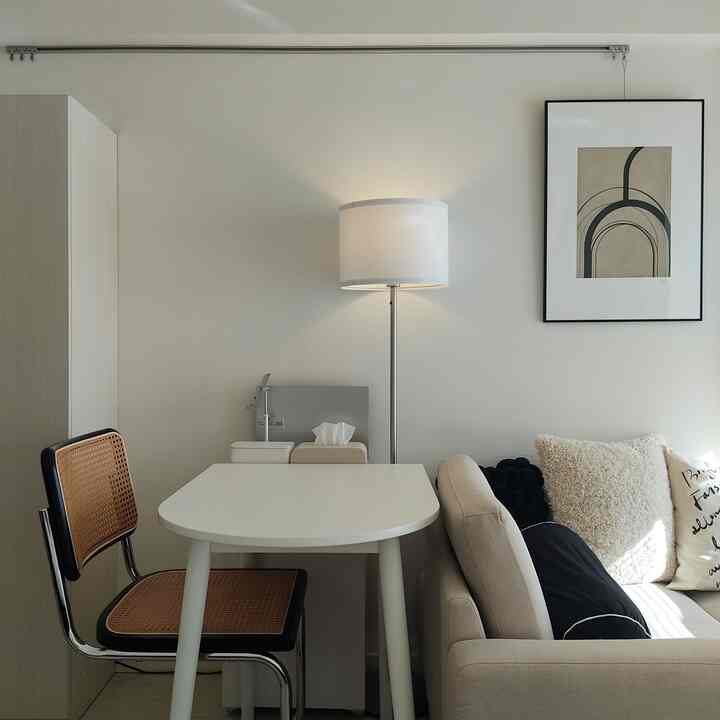 ベージュとホワイトのトーンが特徴の1Kアパートの一人暮らし用リビング・ダイニング空間、シンプルなテーブルとラタンチェア、フロアランプが配置された自然でモダンなインテリア