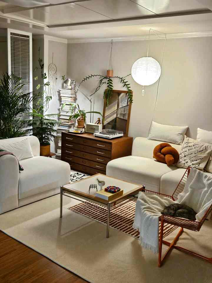 白と木目調が調和した居心地の良いリビング、2つのソファとアームチェア、多数の植物が配された落ち着いた空間