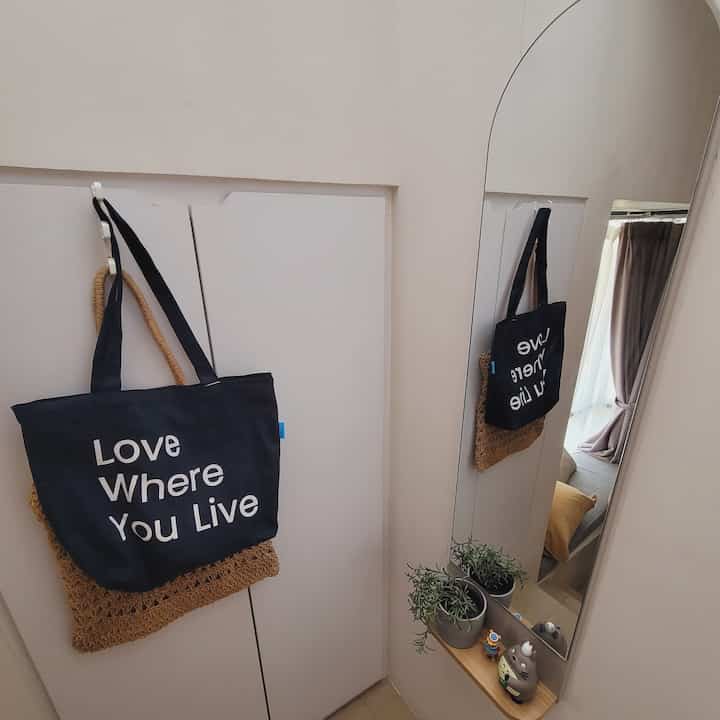 White walls and wood tone shelf in an entrance area with hanging bags and a tall mirror, creating a cozy atmosphere