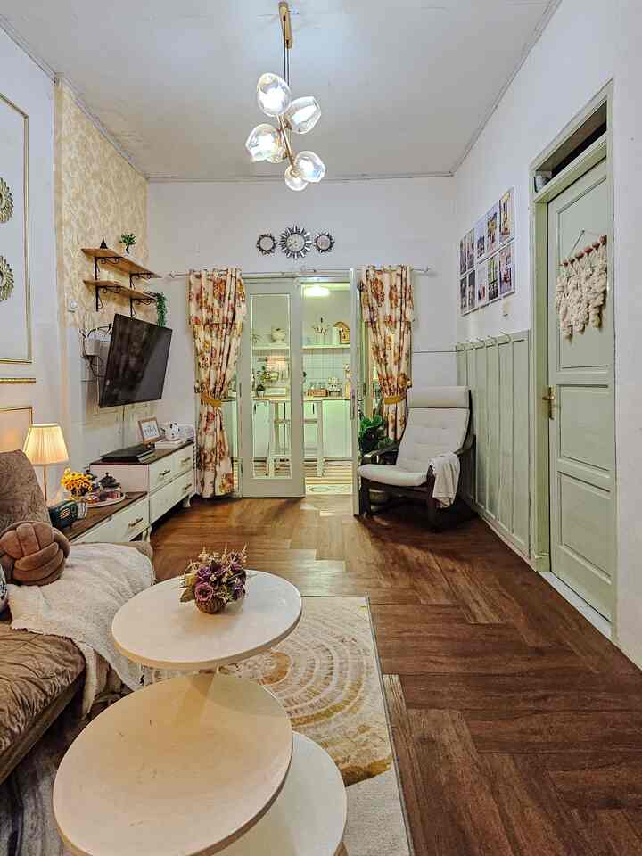 Cozy living room connected to kitchen featuring warm wood flooring, white walls, minimalist furniture and floral curtains