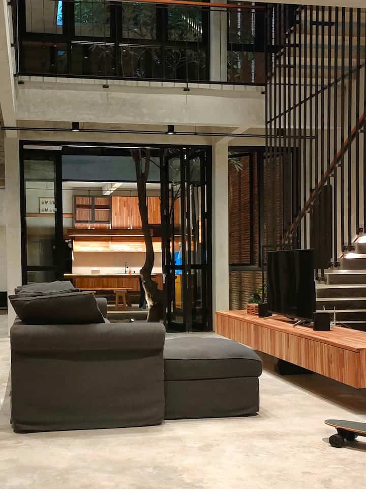 Modern living room featuring grey sofa and TV stand with concrete floor and staircase, showcasing an open plan design