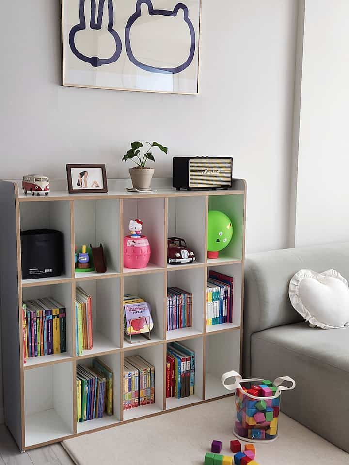 白と自然の色調のリビング、幼児用本棚とソファが配置された清潔で落ち着いたインテリア