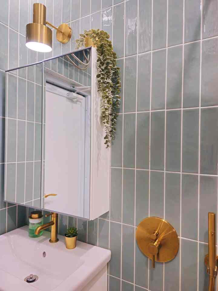 Bathroom with green tiled walls and gold fixtures, featuring a mirror cabinet and sink creating a clean and elegant space