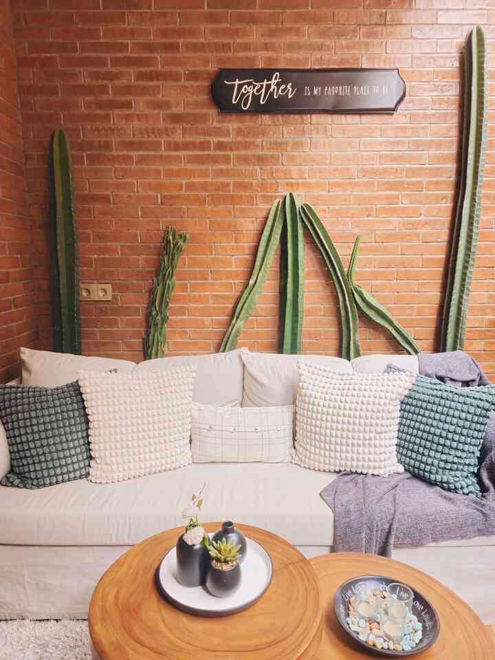Warm brown brick wall natural-toned living room featuring beige sofa with assorted cushions creating a cozy atmosphere