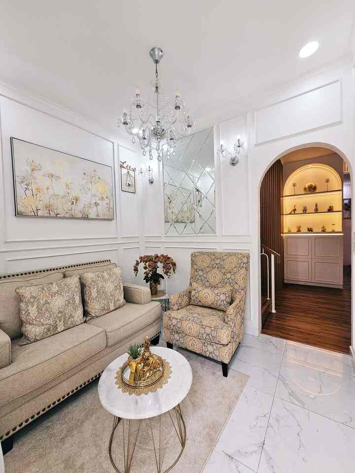 A modern living room with white and beige tones featuring a chandelier, patterned armchair, marble coffee table, and elegant decor