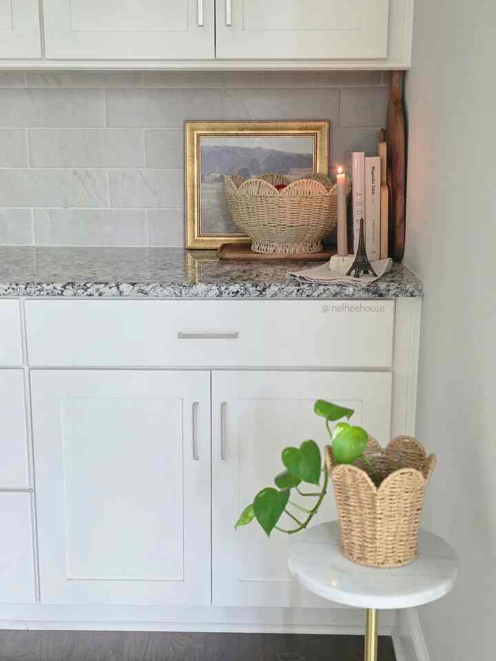 Natural white and brown toned kitchen corner featuring plants, candle, and woven baskets with a cozy atmosphere