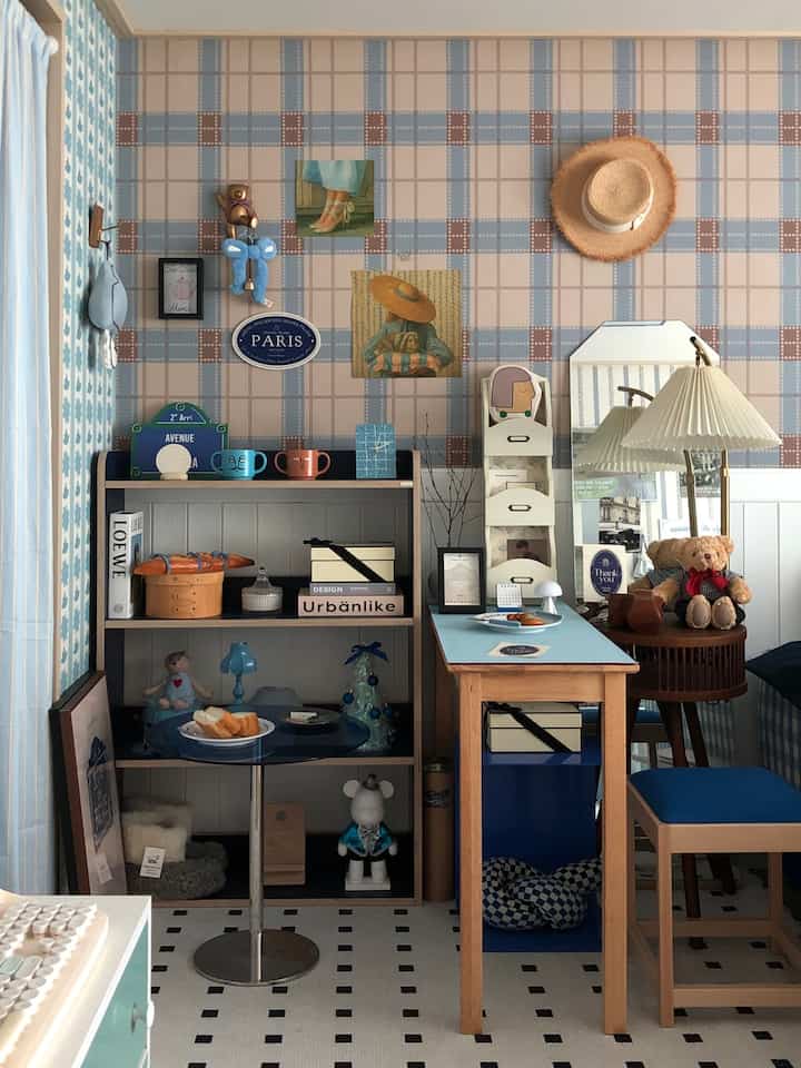 ブルーとウッドトーンが調和する寝室、木製家具とフレンチテイストのポスター、チェックパターンの壁紙によるヴィンテージスタイルのインテリア
